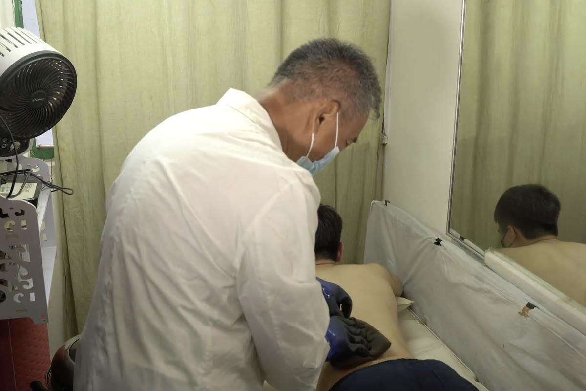 Tiến sĩ Tse See-li điều trị chứng ứ máu cho bệnh nhân bằng cách đắp một gói thuốc thảo dược nóng lên vùng bị đau, hình ảnh được trích từ loạt video “Trăm bệnh trăm thuốc”. (Ảnh chụp màn hình qua YouTube/GreenEastern)