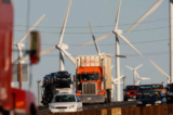 Xe hơi và xe tải xả khí thải đi qua một trang trại phong năng dọc theo đường xa lộ California. Người Mỹ bị phân cực sâu sắc trong niềm tin về biến đổi khí hậu, và các nhà nghiên cứu muốn biết lý do tại sao. (Ảnh: David McNew/Getty Images)