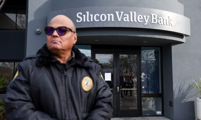 Một nhân viên bảo vệ tại ngân hàng Silicon Valley Bank đã phá sản theo dõi một hàng người bên ngoài văn phòng ở Santa Clara, California, hôm 13/03/2023. (Ảnh: Justin Sullivan/Getty Images)