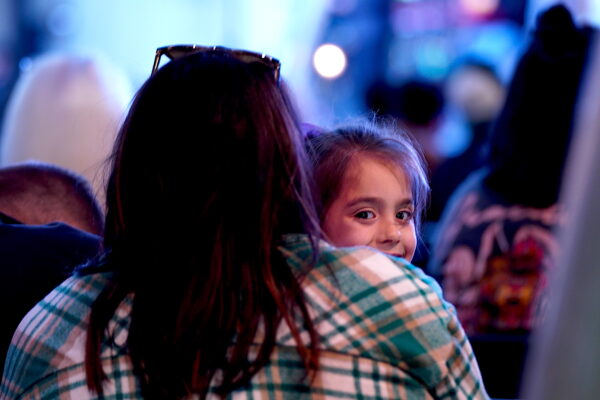 Một bé gái mỉm cười trong vòng tay của mẹ trong một buổi thánh lễ được tổ chức ngoài trời ở Bakersfield, California, hôm 12/03/2023. (Ảnh: Allan Stein/The Epoch Times)