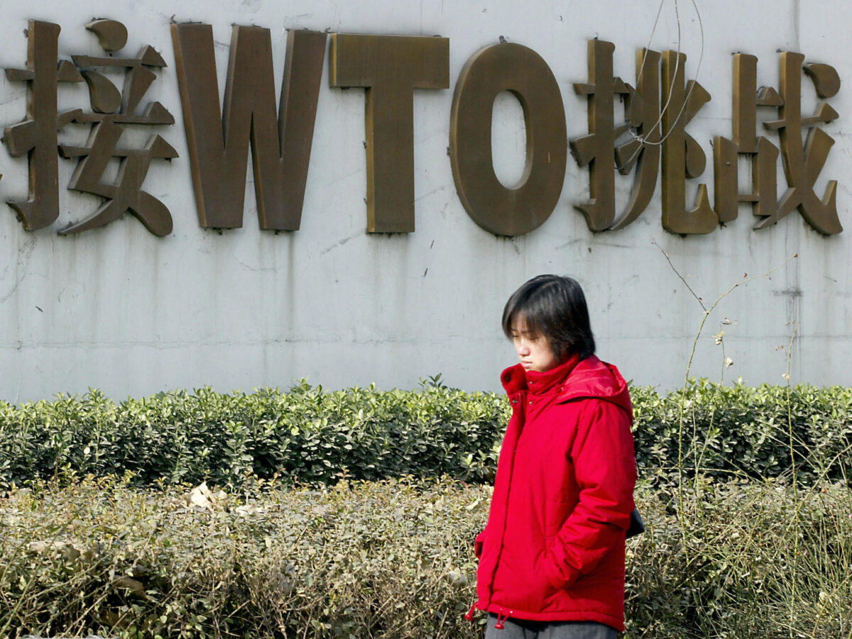 Một phụ nữ Trung Quốc đi ngang qua một tấm biển quảng cáo việc Trung Quốc được trở thành thành viên của Tổ chức Thương mại Thế giới (WTO) dọc theo con đường ở Bắc Kinh vào ngày 19/12/2003. (Ảnh: Goh Chai Hin/AFP/Getty Images)