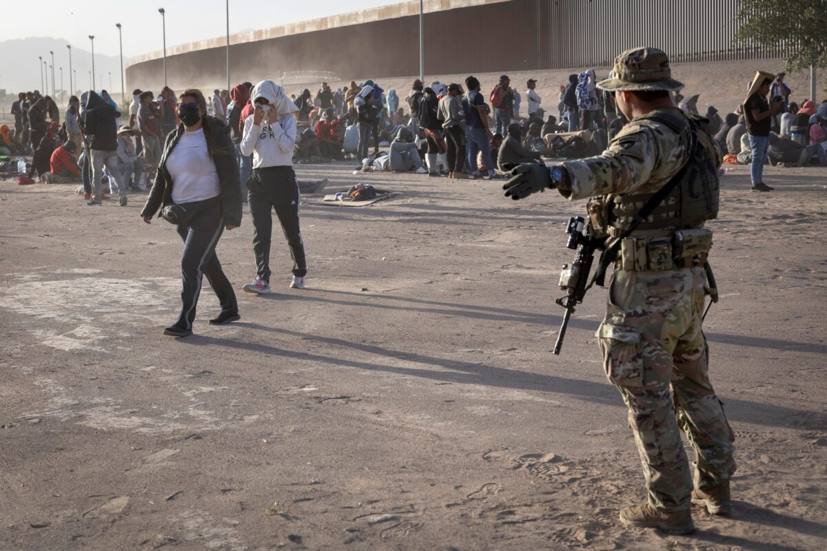 Một người lính Vệ binh Quốc gia Texas chỉ dẫn cho những người nhập cư trong một cơn bão bụi tại một trại di cư dã chiến nằm giữa Rio Grande và hàng rào biên giới Hoa Kỳ-Mexico ở El Paso, Texas, hôm 10/05/2023. (Ảnh: John Moore/Getty Images)