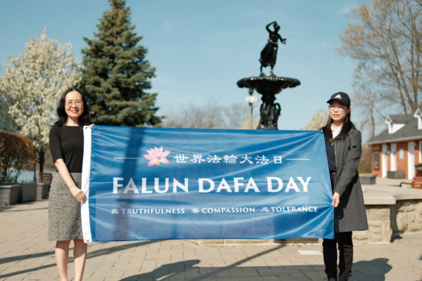 Các học viên Pháp Luân Công Carolyn Jin (trái) và Melissa Li cầm cờ Pháp Luân Đại Pháp tại Tòa thị chính Hamilton ở Ontario hôm 05/05/2023, để kỷ niệm 31 năm Ngày Pháp Luân Đại Pháp Thế Giới. (Ảnh: The Epoch Times)