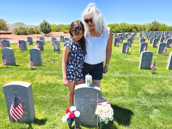 Bà Diana Espinosa (phải) và cháu gái đặt một tách cà phê đen trước bia mộ của người chồng quá cố của bà Diana, cựu chiến binh Hải quân Hoa Kỳ Ernest Arsenio Espinosa, người đã qua đời vào ngày 11/08/2019. Ông yên nghỉ với đầy đủ danh hiệu quân sự tại Nghĩa trang Tưởng niệm Cựu chiến binh Arizona ở Marana, Arizona. Bức ảnh được chụp hôm 27/05/2023. (Ảnh: Allan Stein/The Epoch Times)