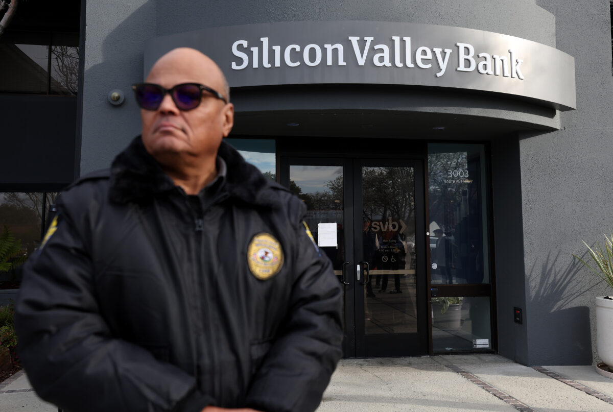 Một nhân viên bảo vệ tại ngân hàng Silicon Valley Bank bị phá sản đang trông chừng một hàng người bên ngoài văn phòng ở Santa Clara, California, hôm 13/03/2023. (Ảnh: Justin Sullivan/Getty Images)