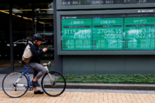 Một người đàn ông đi xe đạp đậu xe trước bảng điện tử hiển thị chỉ số chứng khoán Thượng Hải, chỉ số giá cổ phiếu Nikkei và Chỉ số Trung bình Công nghiệp Dow Jones bên ngoài một công ty môi giới ở Tokyo, Nhật Bản, hôm 22/09/2022. (Ảnh: Kim Kyung-Hoon/Reuters)