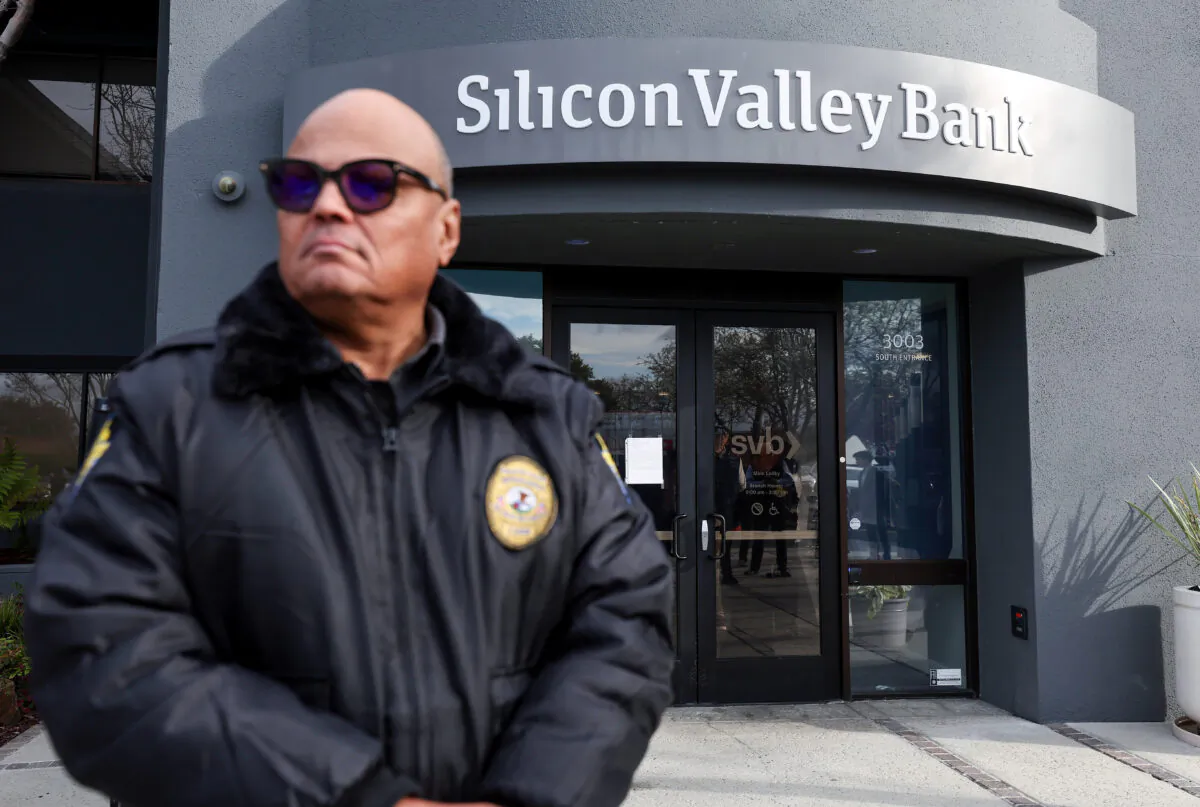 Một nhân viên bảo vệ tại ngân hàng đã sụp đổ Silicon Valley Bank theo dõi hàng người bên ngoài văn phòng ở Santa Clara, California, hôm 13/03/2023. (Ảnh: Justin Sullivan/Getty Images)
