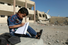 Một cậu học trò người Yemen ngồi viết bài bên ngoài một ngôi trường bị hư hại trong một cuộc không kích ở thành phố Taez, miền nam Yemen, vào ngày 16/03/2017. (Ảnh: Ahmad Al-Basha/AFP qua Getty Images)