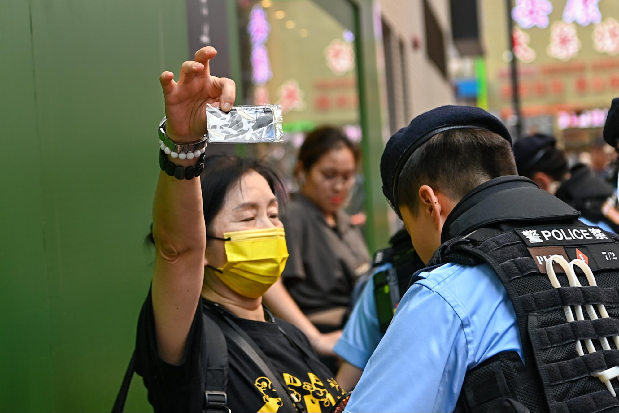 Một người phụ nữ đeo khẩu trang màu vàng đang giơ một tấm thẻ ghi chữ “Lương tâm” khi bị cảnh sát khám xét. (Ảnh: Sung Pi-lung/The Epoch Times)