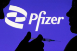 Hình ảnh một người tạo dáng với ống chích trước logo Pfizer Inc. vào ngày 11/12/2021. (Ảnh: Dado Ruvic/Reuters)