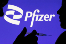 Hình ảnh một người tạo dáng với ống chích trước logo Pfizer Inc. vào ngày 11/12/2021. (Ảnh: Dado Ruvic/Reuters)