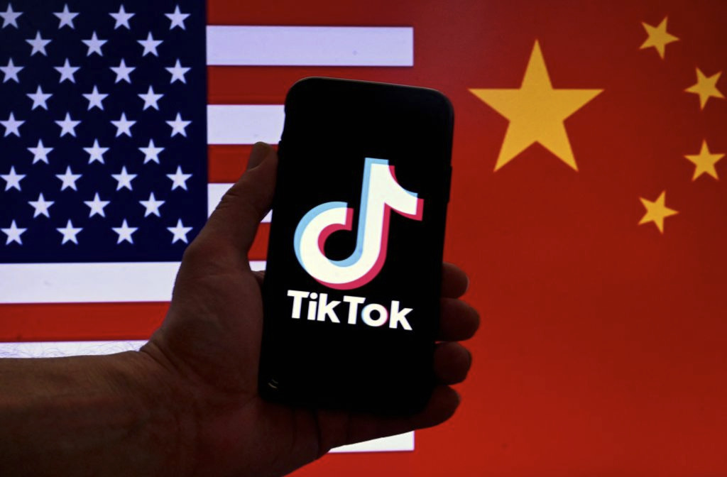 Logo của ứng dụng mạng xã hội TikTok hiển thị trên màn hình iPhone, trước nền quốc kỳ của Hoa Kỳ và Trung Quốc tại Hoa Thịnh Đốn hôm 16/03/2023. (Ảnh: Olivier Douliery/AFP qua Getty Images)