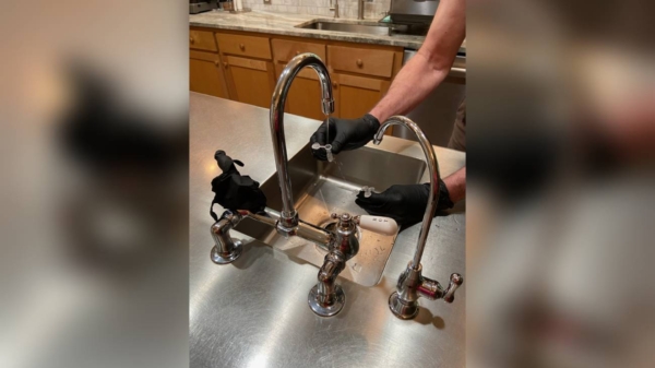 Một khoa học gia của USGS đeo găng tay màu đen đang lấy mẫu nước từ bồn rửa nhà bếp bằng cách sử dụng các lọ nhựa nhỏ để kiểm nghiệm hóa chất PFAS. (Ảnh: Paul Bradley/USGS)