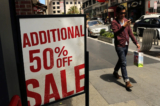 Một khách bộ hành cầm một chiếc túi mua sắm đi ngang qua biển hiệu giảm giá tại một cửa hàng quần áo bán lẻ ở San Francisco hôm 13/05/2013. (Ảnh: Robert Galbraith/Reuters)