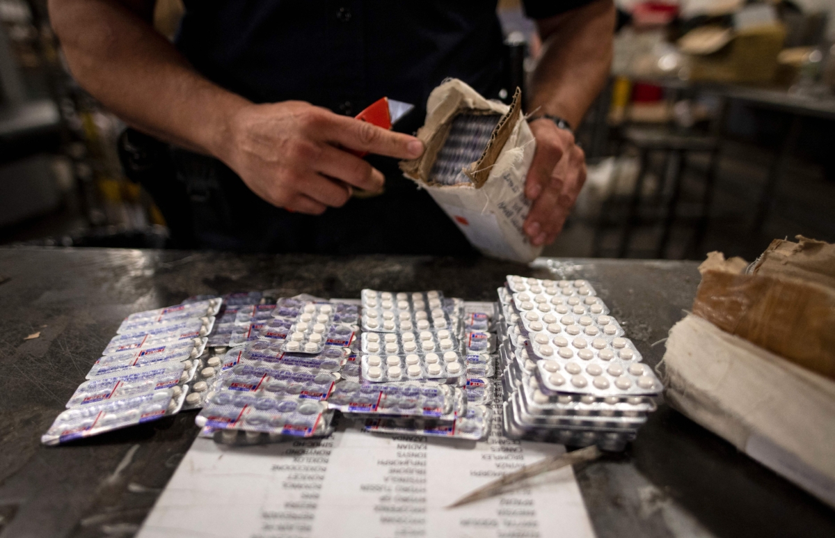 Một nhân viên thuộc Phòng Thương mại và Hàng hóa của Cục Hải quan và Biên phòng Hoa Kỳ tìm thấy những viên thuốc Oxycodone trong một bưu kiện tại cơ sở Dịch vụ Bưu chính Hoa Kỳ của Phi trường John F. Kennedy ở New York vào ngày 24/06/2019. (Ảnh: Johannes Eisele/AFP qua Getty Images)