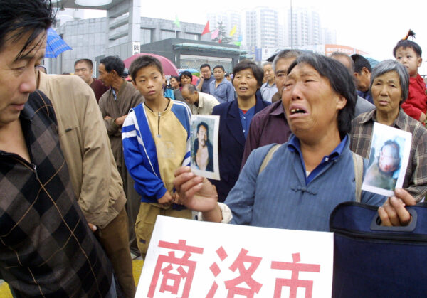 Một người phụ nữ nông dân khóc khi cầm những bức ảnh của con trai mình, người mà bà cho rằng đã bị chính quyền địa phương đánh đập và sát hại, khi bà cùng với những người khiếu kiện khác xếp hàng bên ngoài văn phòng khiếu nại mới ở Tây An, tỉnh Thiểm Tây, miền trung Trung Quốc vào ngày 18/08/2005, để đơn khiếu kiện của họ có cơ hội được tiếp nhận. (Ảnh: STR/AFP qua Getty Images)