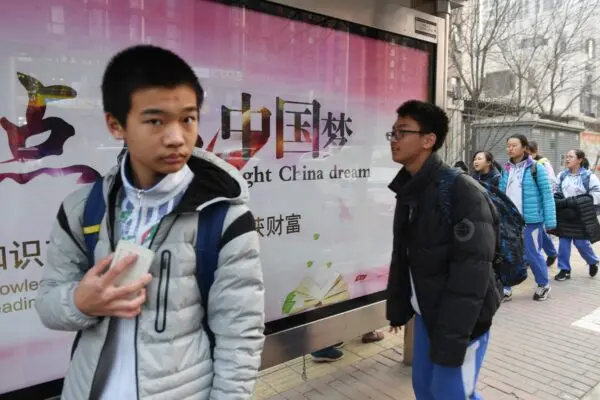 Thanh thiếu niên đi ngang qua một bảng quảng cáo tuyên truyền về “Giấc mộng Trung Hoa,” một khẩu hiệu gắn liền với nhà lãnh đạo Trung Quốc Tập Cận Bình, bên ngoài một trường học ở Bắc Kinh vào ngày 12/03/2018. (Ảnh: Greg Baker/AFP qua Getty Images)