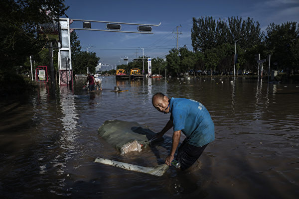 Hôm 05/08/2023, tại thành phố Trác Châu, tỉnh Hà Bắc, một người đàn ông lội qua dòng nước lũ đang rút và kéo theo một chiếc bao chứa đầy vật dụng được trục vớt từ tòa nhà. (Ảnh: Kevin Frayer)