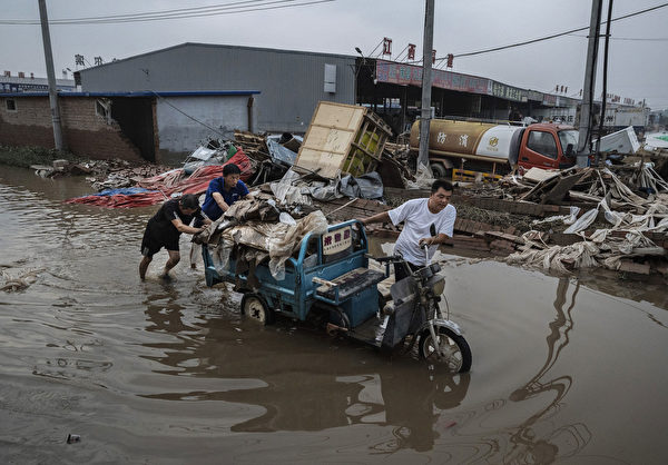 Hôm 05/08/2023, người dân đẩy một chiếc xe ba bánh chở đầy hàng hóa được trục vớt từ một doanh nghiệp địa phương qua dòng nước ở thành phố Trác Châu, tỉnh Hà Bắc, Trung Quốc. (Ảnh: Kevin Frayer/Getty Images）
