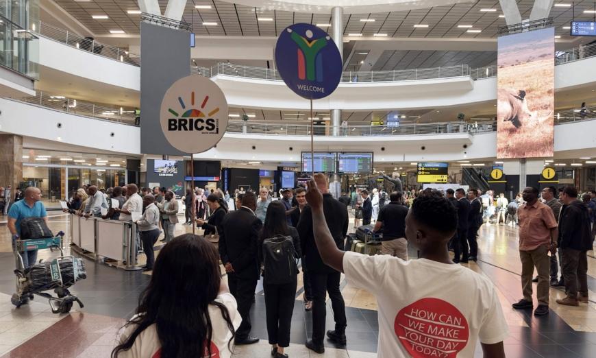Các tình nguyện viên của hội nghị BRICS cầm các tấm biển tại ga đến quốc tế tại Phi trường Quốc tế OR Tambo ở Ekurhuleni, Nam Phi, hôm 21/08/2023. (Ảnh: Marco Longari/AFP qua Getty Images)