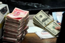 Một nhân viên ngân hàng Trung Quốc chuẩn bị đếm một chồng USD và các xấp tiền giấy 100 nhân dân tệ tại một ngân hàng ở Hợp Phì, tỉnh An Huy, Trung Quốc, hôm 09/03/2010. (Ảnh: STR/AFP qua Getty Images)