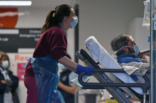 Một chuyên gia y tế mặc đồ bảo hộ cá nhân đẩy bệnh nhân cũng đeo khẩu trang đang nằm trên giường, tại Bệnh viện St Thomas ở phía bắc London, vào ngày 01/04/2020. (Ảnh: Daniel Leal-Olivas/AFP qua Getty Images)