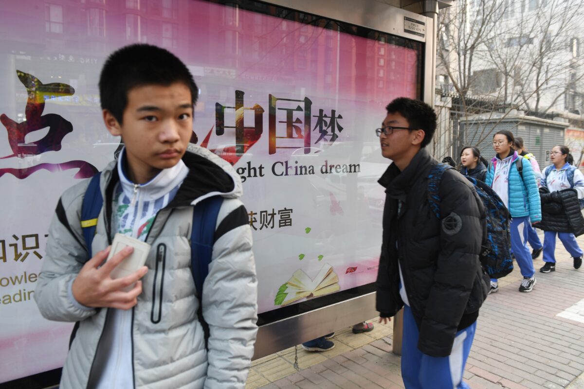 Các thanh thiếu niên đi ngang qua bảng quảng cáo tuyên truyền về “Giấc mộng Trung Hoa,” một khẩu hiệu gắn liền với lãnh đạo Trung Quốc Tập Cận Bình, bên ngoài một trường học tại Bắc Kinh vào ngày 12/03/2018. (Ảnh: Greg Baker/AFP qua Getty Images)