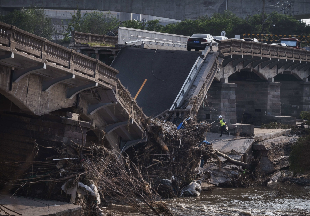 Những chiếc xe hơi bị bỏ phế khi một công nhân kiểm tra một cây cầu bị sập trong những ngày vừa qua sau trận lũ quét do mưa lớn ở Bắc Kinh hôm 04/08/2023. Trận mưa vô cùng lớn từ cơn bão Doksuri là trận mưa lớn nhất đổ bộ vào Bắc Kinh trong 140 năm qua, làm ngập lụt khu vực Bắc Kinh và gây ra lũ quét và lở đất. (Ảnh: Kevin Frayer/Getty Images)