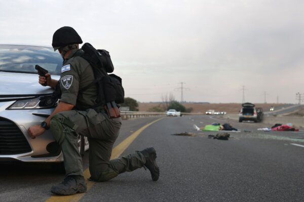 Một người lính Israel nấp sau một chiếc xe hơi sau khi những kẻ khủng bố Hamas tiến vào miền nam Israel và sát hại thường dân. Thi thể người Israel được nhìn thấy ở đây trên con đường chính gần Gevim Kibbutz của Israel, gần biên giới với Gaza hôm 07/10/2023. (Ảnh: Oren Ziv/AFP qua Getty Images)