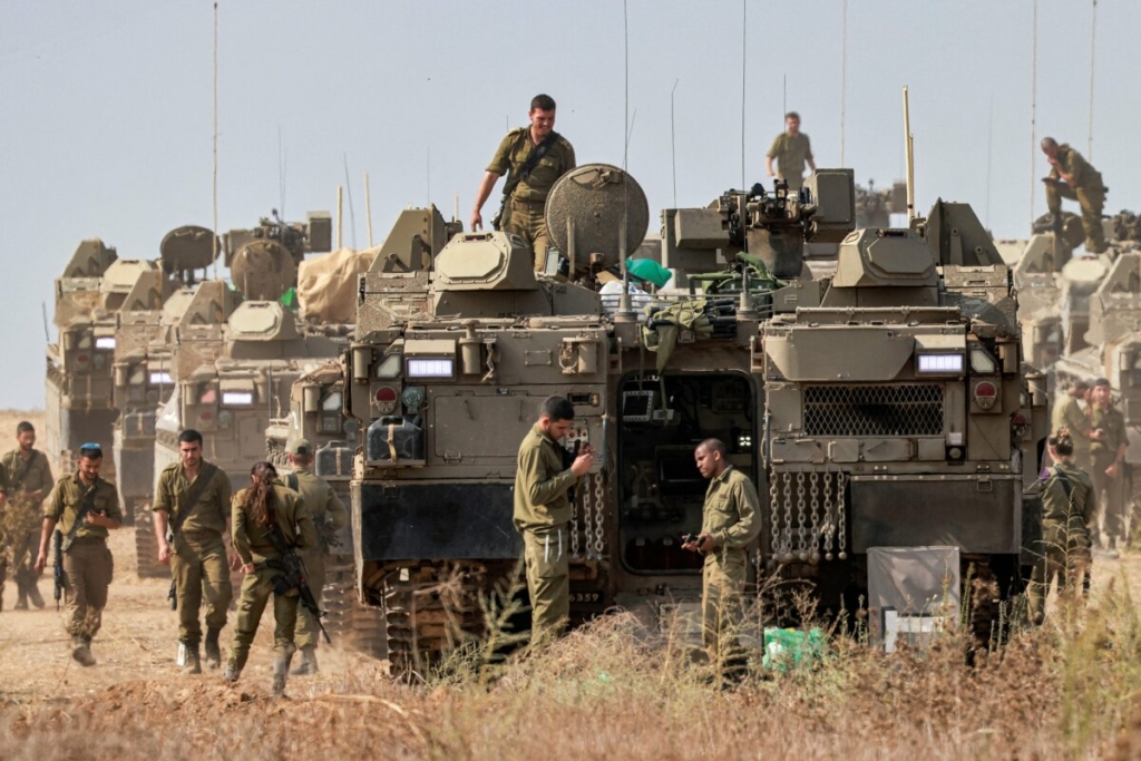 Các binh sĩ quân đội Israel đứng gần các xe bọc thép Namer (APC) đóng quân tại một vị trí gần biên giới với Gaza ở miền nam Israel hôm 11/10/2023. (Ảnh: Menahem Kahana/AFP qua Getty Images)