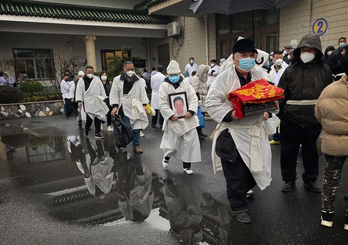 Một người đưa tang ôm tro cốt hỏa táng của người thân cùng những người phúng viếng khác mặc trang phục tang lễ màu trắng truyền thống trong một lễ tang ở Thượng Hải, Trung Quốc, hôm 14/01/2023. (Ảnh: Kevin Frayer/Getty Images)
