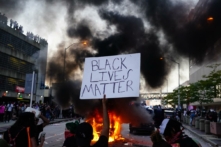 Một người đàn ông cầm tấm biển Black Lives Matter trước một chiếc xe cảnh sát bốc cháy bên ngoài Trung tâm CNN ở Atlanta vào ngày 29/05/2020, trong một cuộc biểu tình sau vụ tử vong của ông George Floyd. (Ảnh: Elijah Nouvelage/Getty Images)
