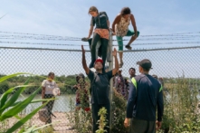 Những người nhập cư bất hợp pháp giúp nhau trèo qua hàng rào thép gai từ Mexico vào Hoa Kỳ, ở Eagle Pass, Texas, hôm 15/08/2023. (Ảnh: Suzanne Cordeiro/AFP qua Getty Images)