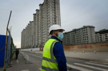 Một công nhân đứng nhìn khi chuẩn bị băng qua đường bên ngoài một công trường xây dựng ở Bắc Kinh hôm 26/04/2022. (Ảnh: Wang Zhao/AFP qua Getty Images)