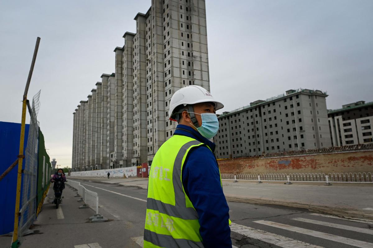Một công nhân quan sát xung quanh để chuẩn bị băng qua đường, bên ngoài một công trường xây dựng ở Bắc Kinh hôm 26/04/2022. (Ảnh: Wang Zhao/AFP qua Getty Images)