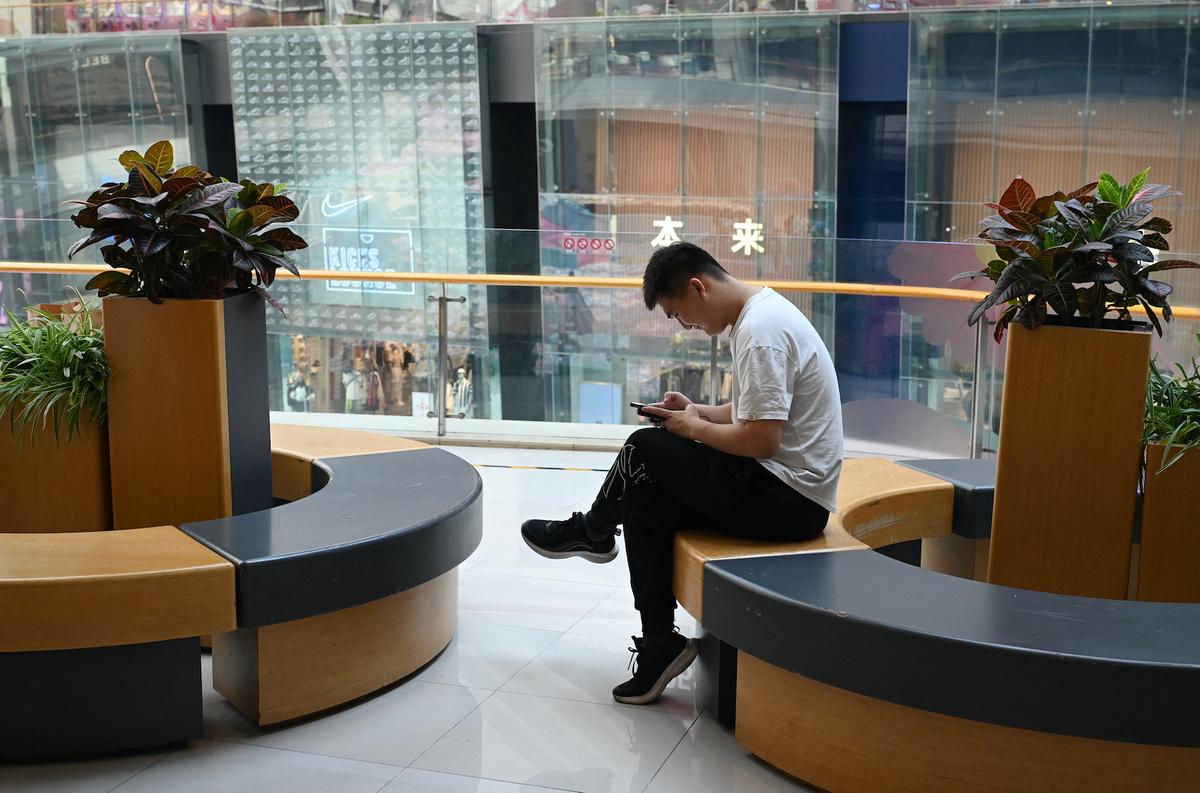 Một người đàn ông xem điện thoại trong lúc nghỉ ngơi tại một trung tâm mua sắm ở Bắc Kinh hôm 18/07/2023. (Ảnh: Greg Baker/AFP qua Getty Images)