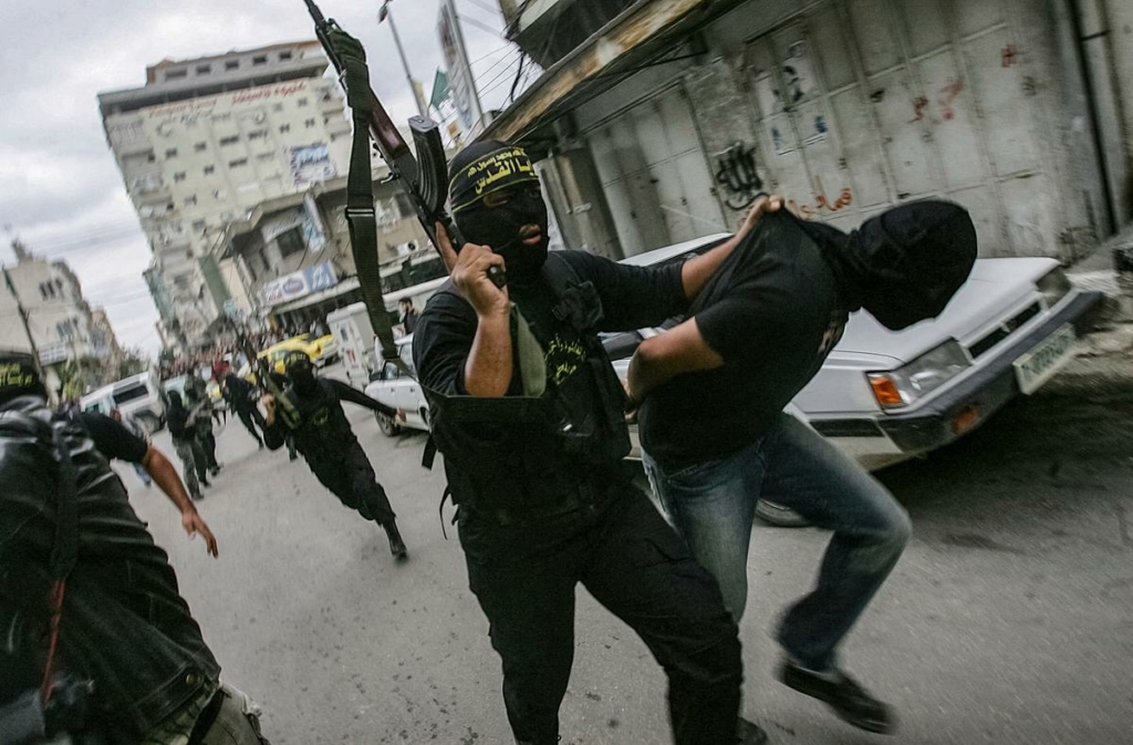 Một kẻ khủng bố người Palestine, một thành viên của phong trào Thánh Chiến Hồi Giáo Jihad, kéo một người đàn ông Palestine bị trùm đầu, người bị cáo buộc là gián điệp cho quân đội Israel, đi qua thành phố Gaza vào ngày 05/11/2006. (Ảnh: Mohammed Abed/AFP qua Getty Images)