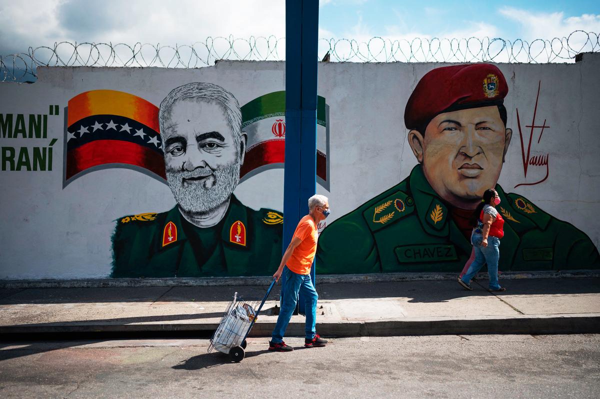 Vài người đang đi ngang qua bức tranh tường vẽ tướng Iran Qasem Soleimani (trái) bị hạ sát, và cố Tổng thống Venezuela Hugo Chavez (phải), tại Caracas, Venezuela, hôm 04/01/2023. (Ảnh: Federico Parra/AFP qua Getty Images)
