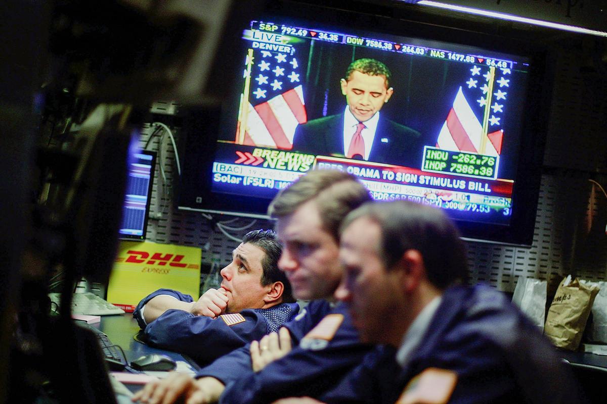 Các giao dịch viên làm việc trên sàn của Sở Giao dịch Chứng khoán New York khi cựu Tổng thống Barack Obama được chiếu trên màn hình tivi tại lễ ký dự luật kích thích kinh tế, ở thành phố New York vào ngày 17/02/2009. Cổ phiếu đã giảm sau khi Tổng thống Obama ký dự luật này. (Ảnh: Mario Tama/Getty Images)