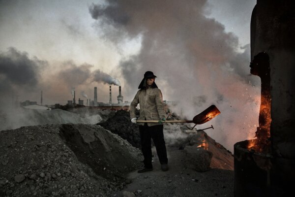Một công nhân Trung Quốc đang chất than vào lò trong lúc khói và hơi nước bốc lên từ một nhà máy thép trái phép ở Nội Mông, Trung Quốc, vào ngày 03/11/2016. (Ảnh: Kevin Frayer/Getty Images)
