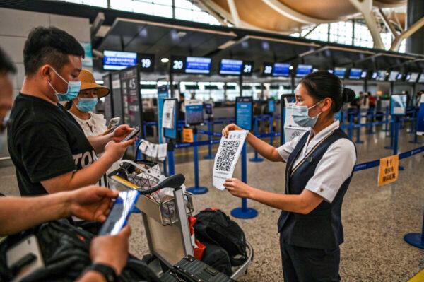 Hành khách đeo khẩu trang cập nhật mã sức khỏe của họ qua một tờ giấy có mã QR do nhân viên phi trường (phải) cầm tại Phi trường Quốc tế Phố Đông ở Thượng Hải, Trung Quốc, vào ngày 11/06/2020. (Ảnh: Hector Retamal/AFP qua Getty Images)