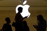 Một người phụ nữ sử dụng thiết bị di động iPhone đi qua một logo Apple đang sáng đèn tại cửa hàng Apple ở Grand Central Terminal, New York, hôm 14/04/2023. (Ảnh: Mike Segar/Reuters)