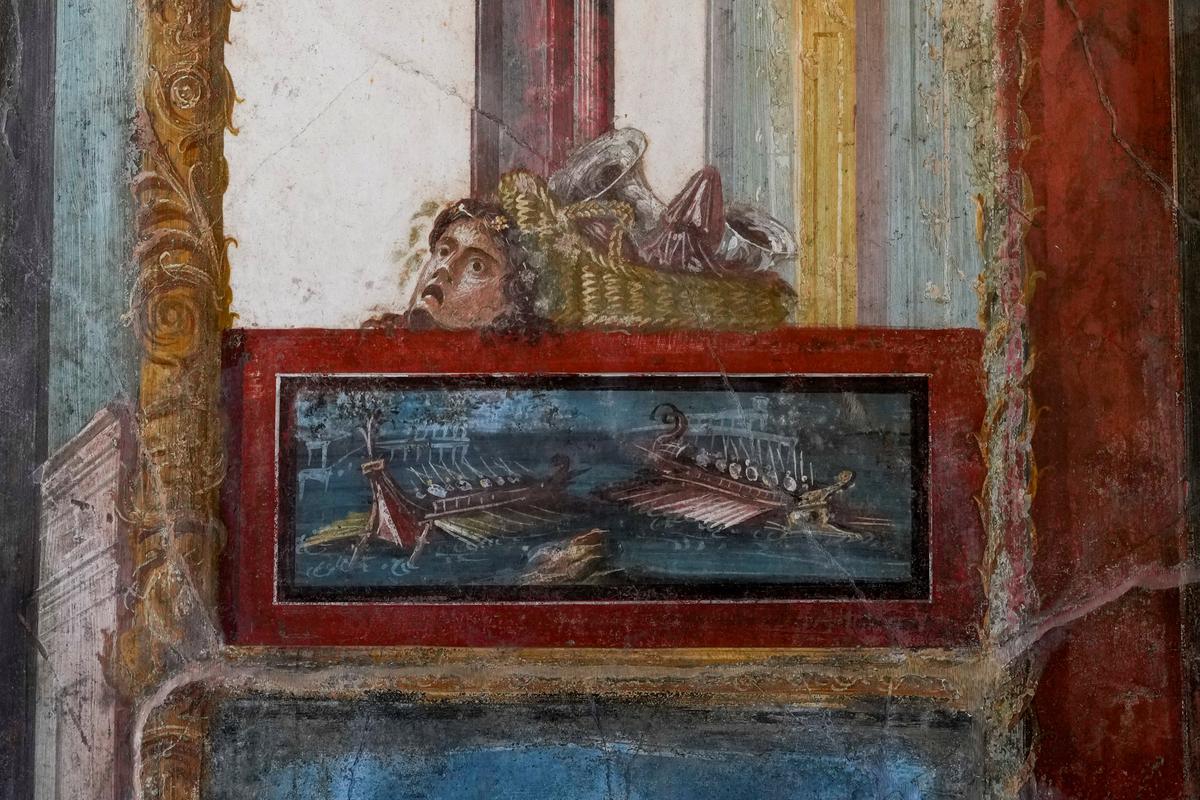 Một phần của bức bích họa mô tả một trận hải chiến được đóng khung màu đỏ Pompeii, phía trên là một chiếc giỏ và một chiếc mặt nạ, trang trí phòng khách trong ngôi nhà của nhà Vetti, một trong những gia đình giàu có nhất ở Pompeii, House of Vetti, trong khu khảo cổ Pompeii, Ý, hôm 07/12/2023. (Ảnh: Andrew Medichini/AP Photo)