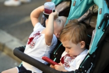 Một em bé chơi điện thoại di động trong khi người anh song sinh uống nước trái cây khi các em tham dự hội trẻ em ở Kiev, ngày 11/08/2018. (Ảnh: Sergei Supinsky/AFP/Getty Images)