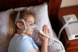 Một cô gái trẻ đeo máy CPAP khi ngủ để điều trị chứng ngưng thở khi ngủ. (Ảnh: Independence_Project/Shutterstock)