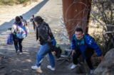 Những người nhập cư bất hợp pháp đi qua một khe hở dọc bức tường biên giới Hoa Kỳ để chờ các nhân viên Tuần tra Biên giới giải quyết ở Jacumba, California, hôm 07/12/2023. (Ảnh: John Fredricks/The Epoch Times)