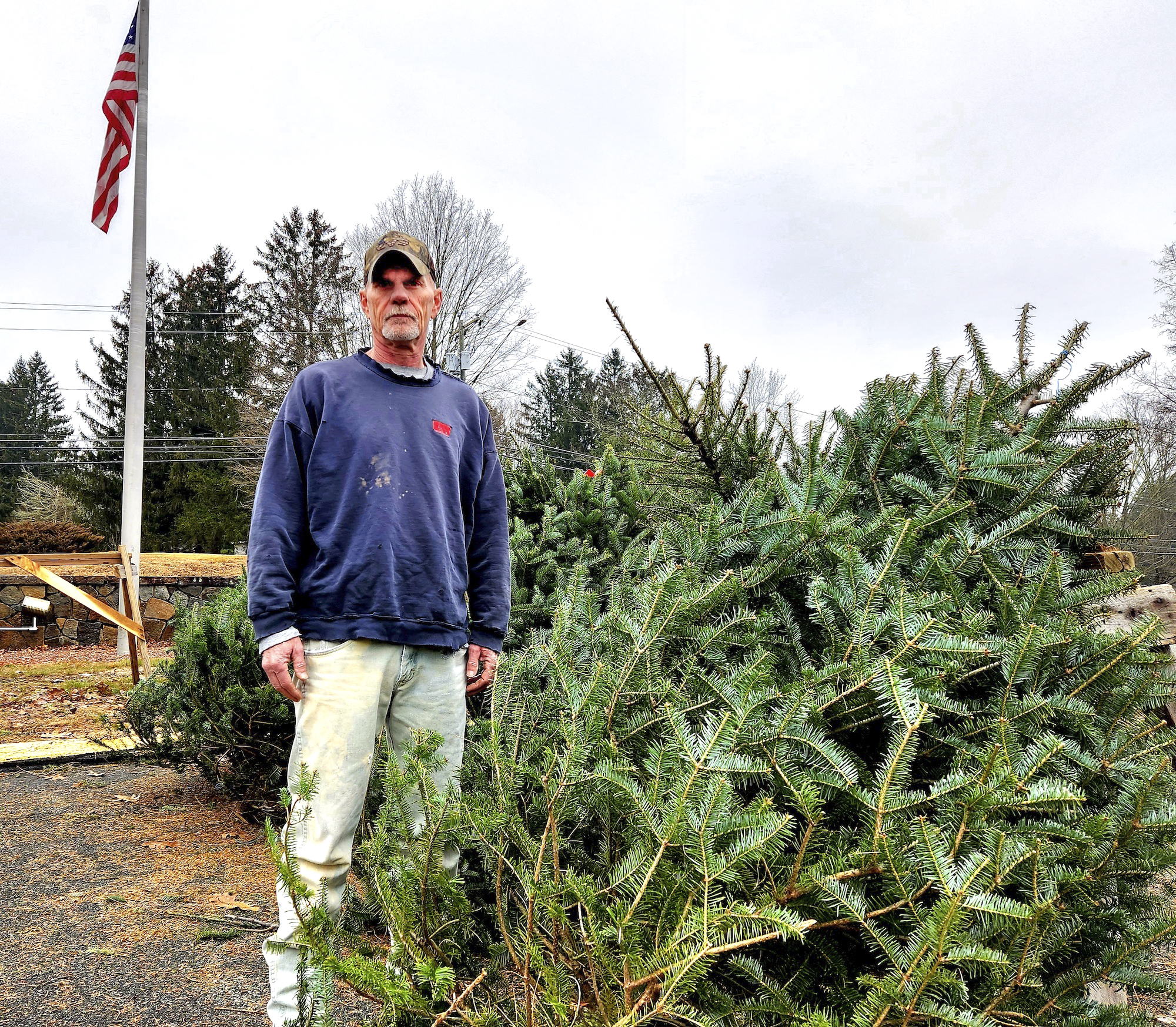 Ông Matt Marella, một lính cứu hỏa tình nguyện, đứng cạnh hàng cây thông Giáng Sinh được bày bán trong một buổi gây quỹ dịp lễ ở Stafford Springs, Connecticut, hôm 10/12/2023. (Ảnh: Allan Stein/The Epoch Times)