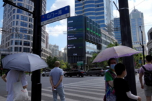 Người đi bộ chờ băng qua đường tại ngã ba gần một màn hình chỉ số chứng khoán lớn ở Thượng Hải, Trung Quốc, hôm 03/08/2022. (Ảnh: Aly Song/Reuters)