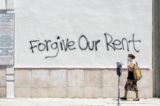 Một người phụ nữ đeo khẩu trang đi ngang qua bức tường có một dòng chữ graffiti yêu cầu bỏ qua tiền thuê nhà trên Đại lộ La Brea ở Los Angeles hôm 01/05/2020. (Ảnh: Valerie Macon/AFP qua Getty Images)