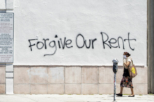 Một người phụ nữ đeo khẩu trang đi ngang qua bức tường có một dòng chữ graffiti yêu cầu bỏ qua tiền thuê nhà trên Đại lộ La Brea ở Los Angeles hôm 01/05/2020. (Ảnh: Valerie Macon/AFP qua Getty Images)